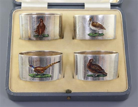 A cased set of four George V silver and enamel serviette rings, each decorated with game birds, 56mm.